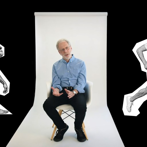 A man sits on a chair in a photo studio, flanked by black-and-white illustrations of an early human ancestor on the left and a modern man running on the right.