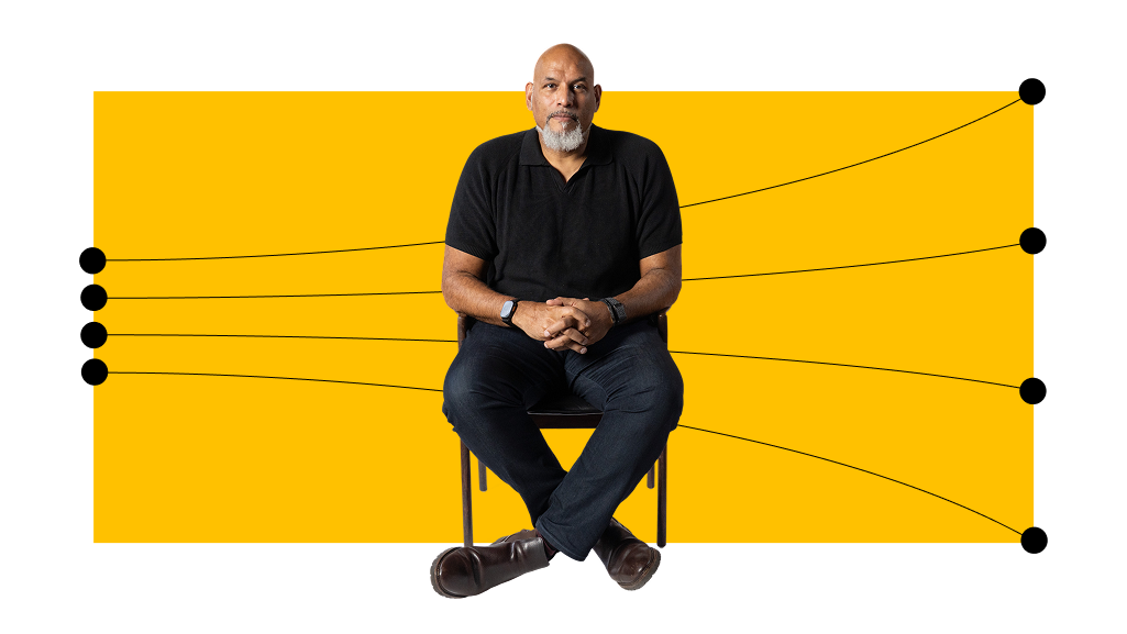 A man with a bald head and beard sits on a chair with arms resting on his lap, in front of a yellow rectangle with black lines and dots extending outward.