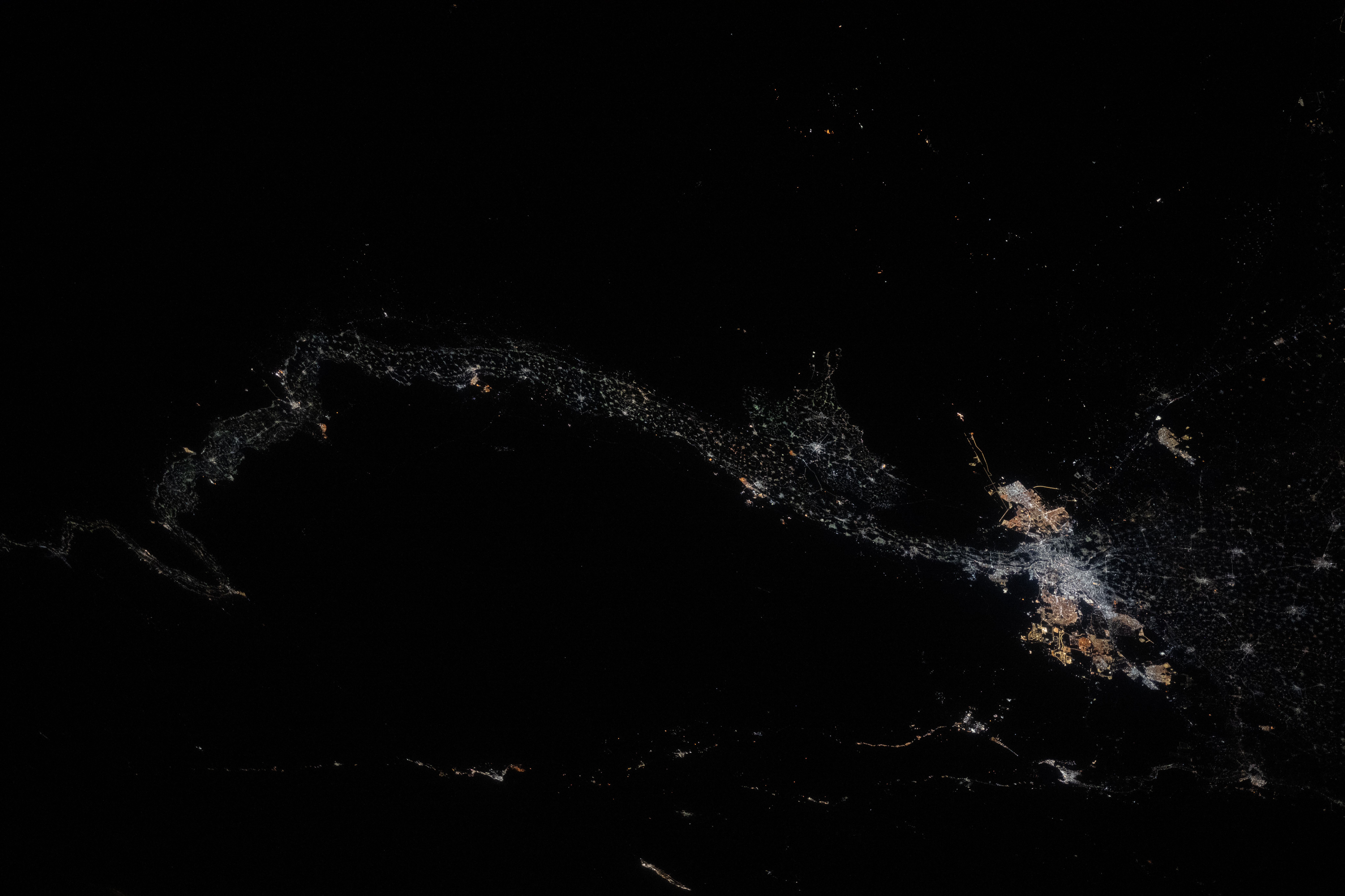 Aerial view of a city at night with illuminated streets and urban areas surrounded by darkness.