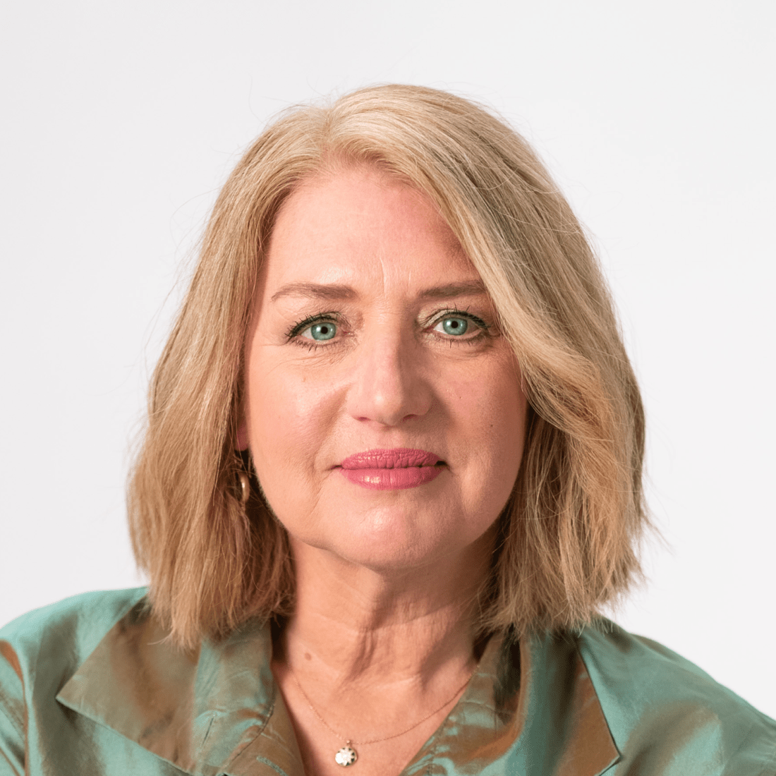 A middle-aged woman with shoulder-length blonde hair wearing a green blouse, looking directly at the camera against a plain white background.
