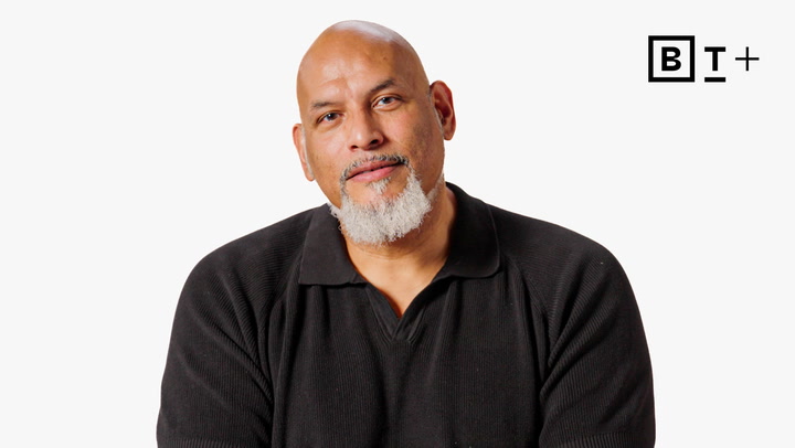 A bald man with a salt-and-pepper goatee wearing a black shirt sits against a plain white background with a "B T +" logo in the top right corner.