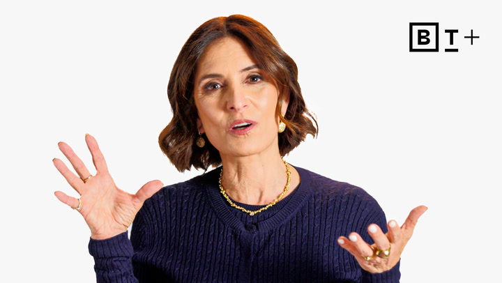 A woman with short brown hair wearing a navy sweater and gold jewelry gestures with her hands in front of a plain white background with a "BT+" logo.