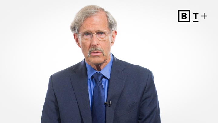 A man in a blue suit and tie stands against a plain white background with a BT+ logo in the top right corner.