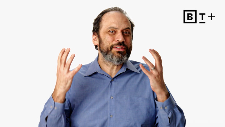 A man with a beard, wearing a blue button-up shirt, gestures with both hands raised. The B+ logo is visible in the top right corner against a white background.