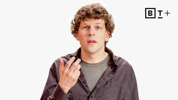 A man with curly hair wearing a gray t-shirt and dark button-up shirt gestures with his hand. A "BT+" logo appears in the corner on a plain white background.