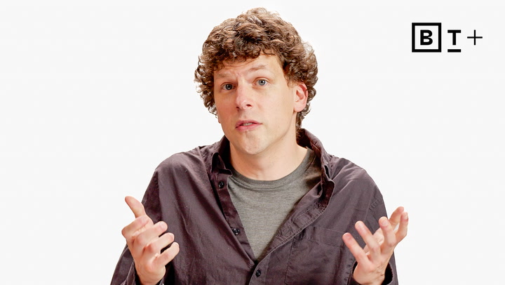 A man with curly hair wearing a dark shirt gestures with both hands in front of a white background with a "BT+" logo in the top right corner.