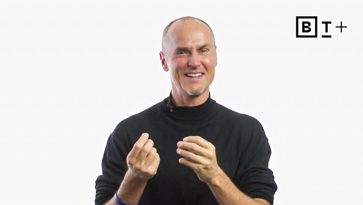 A man in a black turtleneck smiles and gestures with his hands against a plain white background with a "B T+" logo in the top right corner.
