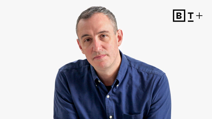 A person with short gray hair wearing a blue button-up shirt sits in front of a white background with a "BT+" logo in the top right corner.