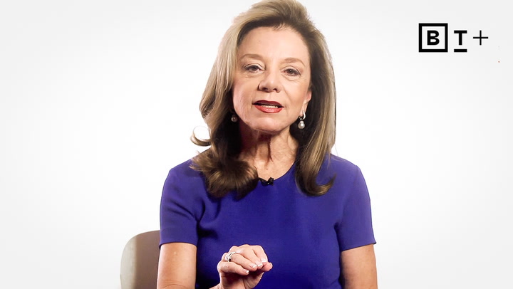A woman with shoulder-length brown hair, wearing a blue dress, speaks while seated against a white background with a BT+ logo in the top right corner.