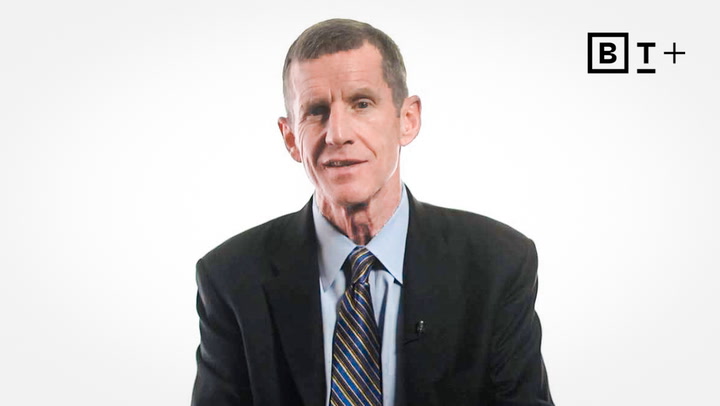 A man in a dark suit and striped tie sits against a plain white background. The letters "BT+" appear in the top right corner.