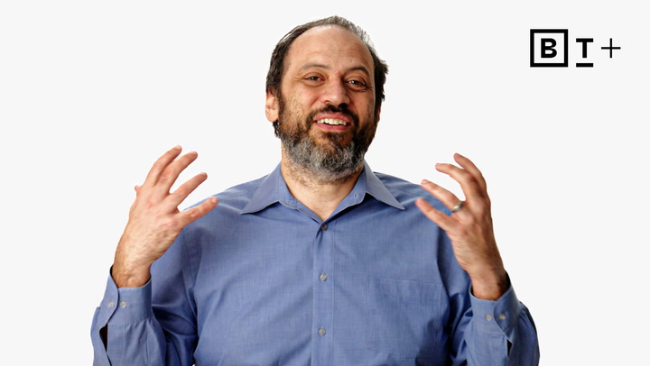 A man with a beard and mustache in a blue shirt gestures with both hands while smiling, with a "B T +" logo in the top right corner.