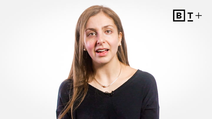 A woman with long brown hair and a black top speaks in front of a white background with a "BT+" logo in the top right corner.
