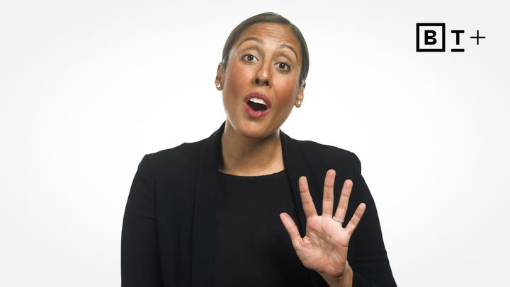 A person in a black blazer gestures with their hand raised, palm facing forward, against a plain white background with a "BT+" logo in the top right corner.