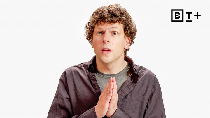 A person with curly hair and a neutral expression holds their hands together, standing in front of a white background with the letters "B T +" in the corner.