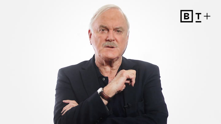 An older man with white hair and a mustache wears a dark suit jacket, standing against a plain white background with a "BT+" logo in the top right corner.