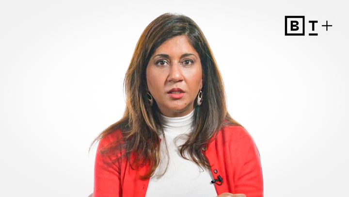 Woman with long dark hair wearing a white turtleneck and red cardigan sits in front of a plain white background with a BT+ logo in the top right corner.