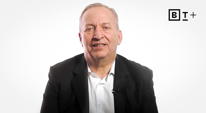 A man in a dark suit jacket and white shirt sits facing the camera against a white background with a "B T+" logo in the top right corner.
