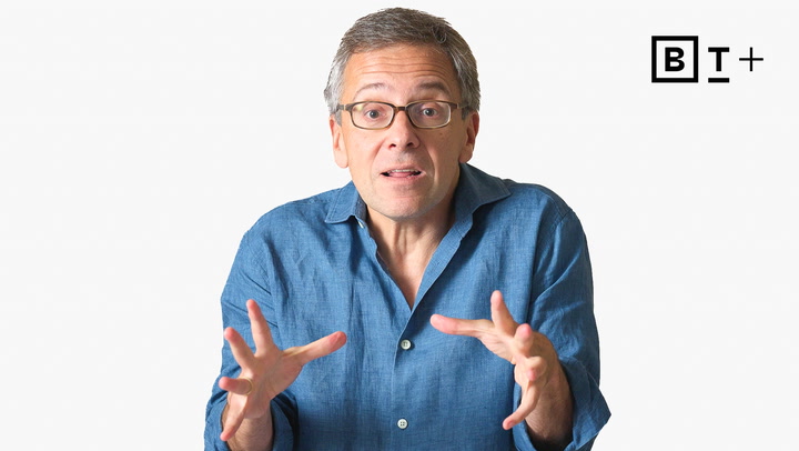 A middle-aged man in glasses and a blue shirt gestures with both hands, looking at the camera. A "B T +" logo is in the upper right corner on a plain white background.