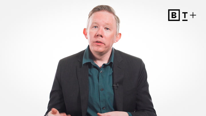 A person in a suit jacket and teal shirt sits in front of a white background with a "B T +" logo in the top right corner.