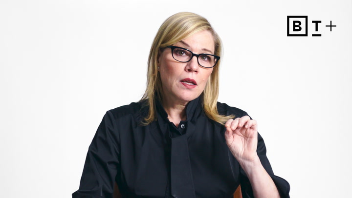 A woman with blonde hair and glasses, wearing a black shirt, speaks while gesturing with her hand. The BT+ logo is visible in the top right corner.