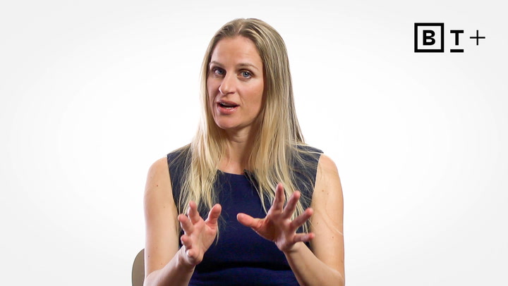 A woman with long blonde hair wearing a sleeveless navy top gestures with her hands while speaking; a "B T +" logo is in the upper right corner.