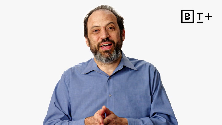 A man with a beard and receding hairline, wearing a blue button-up shirt, stands in front of a white background with a "B T +" logo in the top right corner.