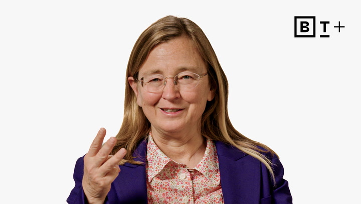 A woman with long blond hair, glasses, and a purple blazer gestures with her hand while speaking. A "B T +" logo appears in the top right corner.