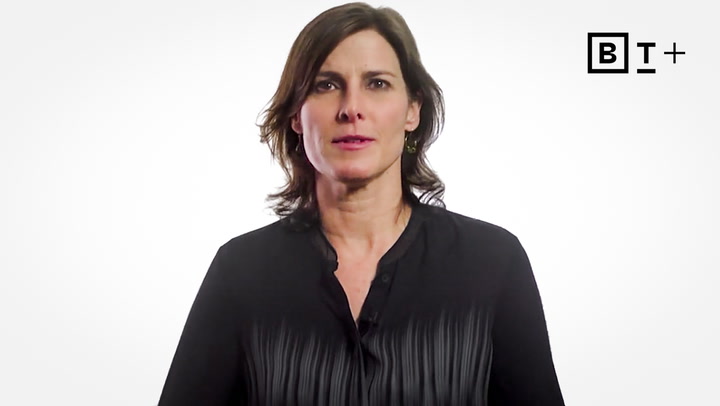 A woman with shoulder-length brown hair wearing a black blouse stands in front of a white background with a “BT+” logo in the top right corner.