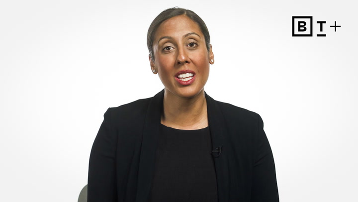 A woman with dark hair pulled back, wearing a black blazer and top, sits in front of a white background with a "BT+" logo in the upper right corner.