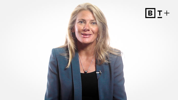 A woman with long blonde hair in a blue blazer sits facing the camera against a white background with a "B T +" logo in the top right corner.