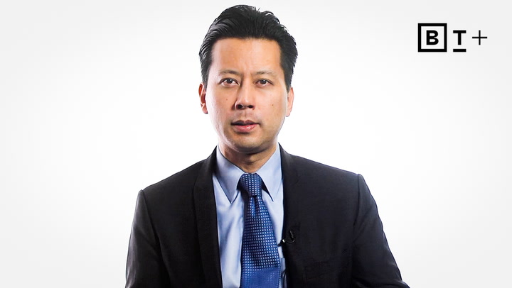A man in a dark suit and blue tie faces the camera against a white background with a "BT+" logo in the top right corner.