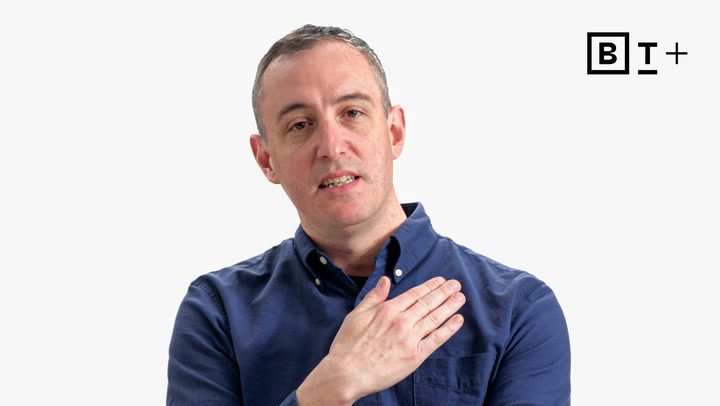 A man in a blue button-up shirt holds his right hand to his chest, standing against a plain white background with a "BT+" logo in the corner.