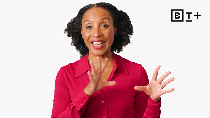 A woman in a bright red blouse gestures with her hands while speaking, standing in front of a plain white background with the "BT+" logo in the top right corner.