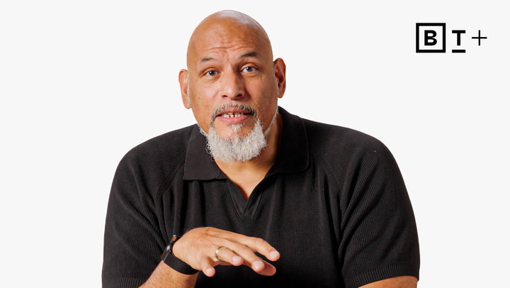 A bald man with a gray goatee, wearing a black polo shirt, gestures with one hand against a white background with a "BT+" logo in the corner.