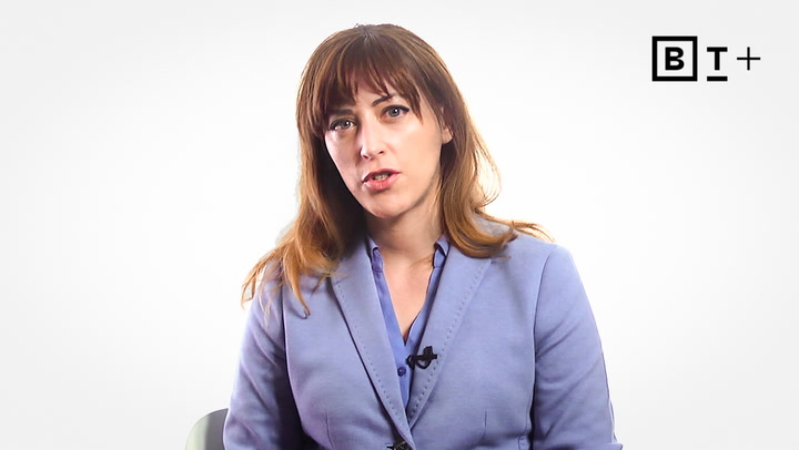 A woman with long brown hair, wearing a light blue blazer, sits against a white background with the BT+ logo in the top right corner.