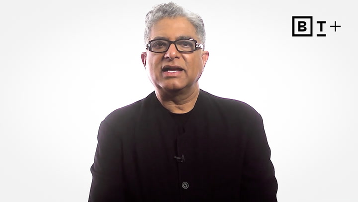 A man wearing glasses and a black jacket speaks in front of a white background with a "B T +" logo in the top right corner.