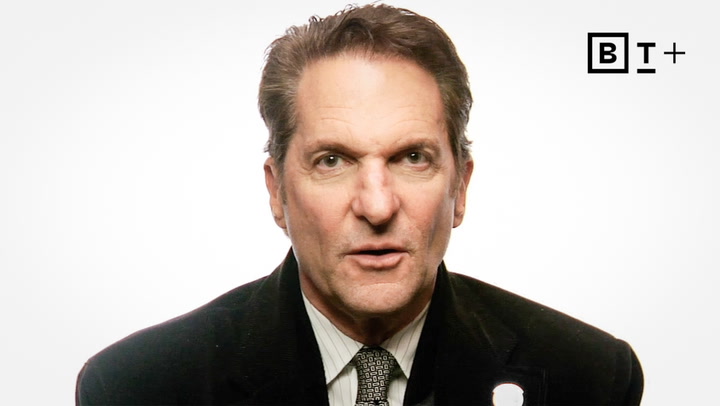 Middle-aged man in a suit and tie facing the camera, with a neutral expression; BT+ logo in the top right corner on a plain white background.