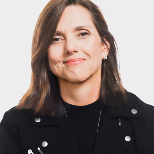 A woman with straight brown hair wearing a black jacket and a black top, smiling slightly, is posing against a plain white background.
