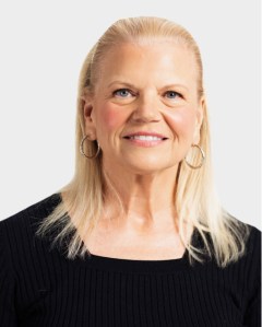 A woman with straight, shoulder-length blonde hair, wearing hoop earrings and a black ribbed top, smiles at the camera against a plain light background.