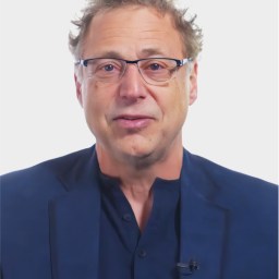 A middle-aged man with light skin, glasses, and short, curly hair is wearing a navy shirt and blazer against a plain white background.