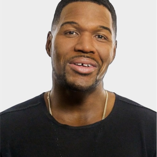 A man with short hair, a trimmed beard, and a black shirt is facing the camera against a plain light background.