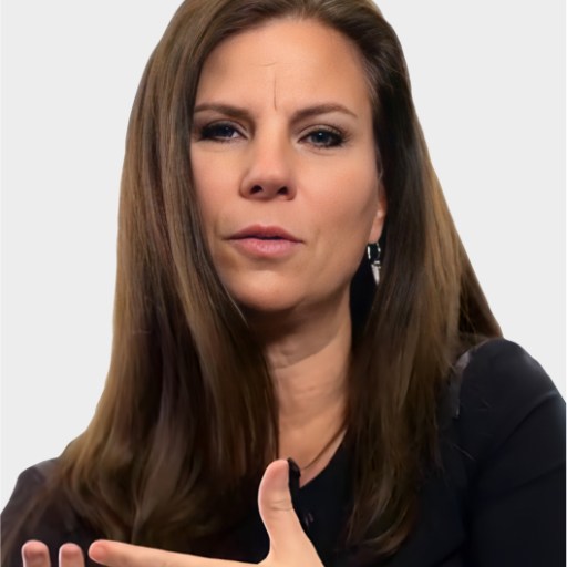 Woman with long brown hair wearing a black top, gesturing with her hand while speaking, against a plain light background.