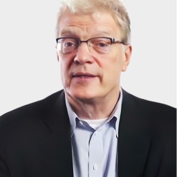 A middle-aged man with light hair and glasses, wearing a dark blazer and light blue shirt, poses against a plain white background.