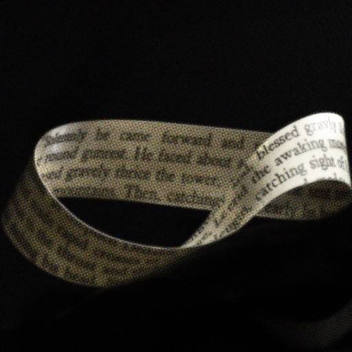 A Möbius strip made from paper with printed text is displayed against a dark background.
