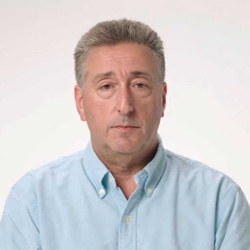 A middle-aged man with short gray hair wearing a light blue button-up shirt faces the camera against a plain light background.