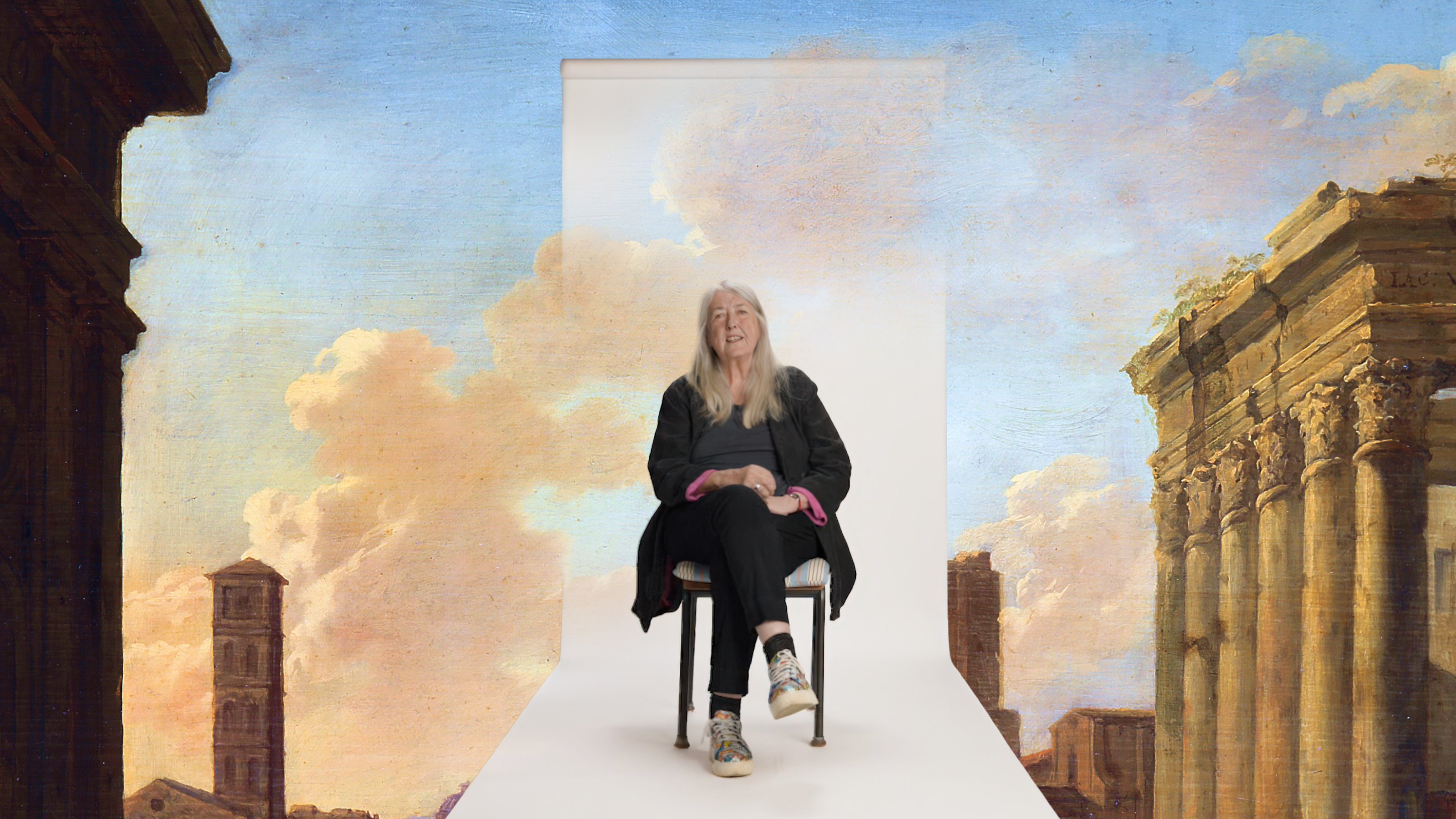 A person with long white hair sits smiling on a chair, set against a painted backdrop of classical architecture and a sky with clouds.