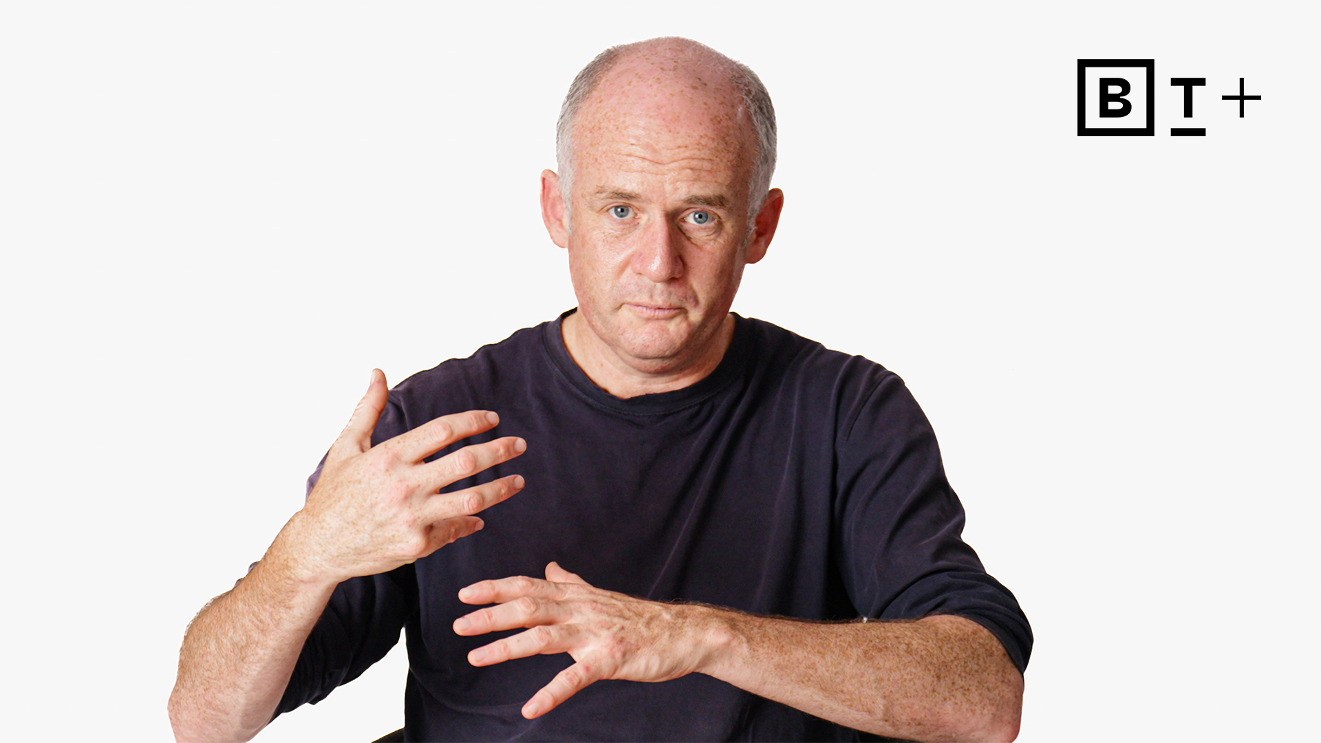 A middle-aged man with a receding hairline gestures with his hands while facing the camera. He wears a dark shirt. A black and white "B T+" logo appears in the upper right corner.