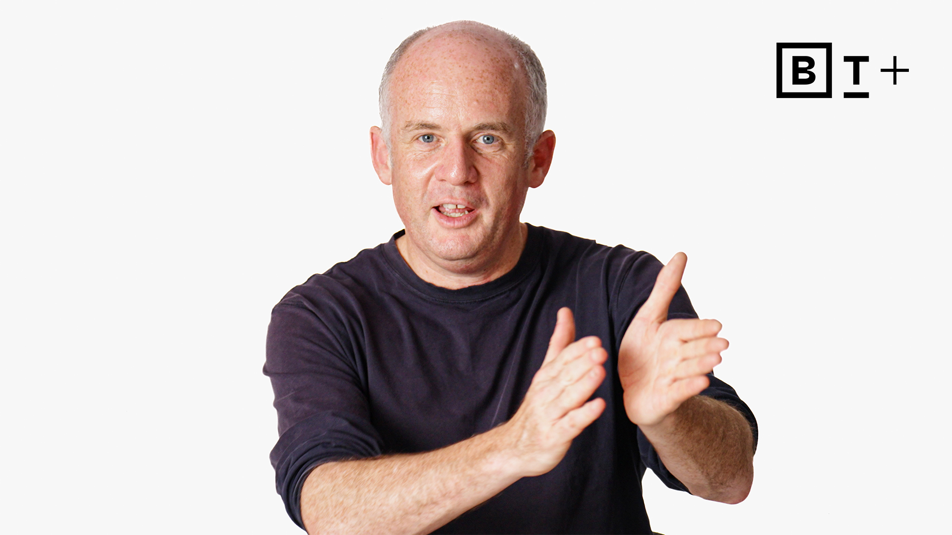 A middle-aged man with short hair wearing a dark shirt gestures with his hands; a "BT+" logo appears in the top right corner on a white background.