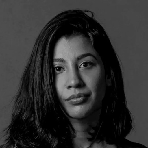 A woman with shoulder-length dark hair looks directly at the camera against a plain gray background.
