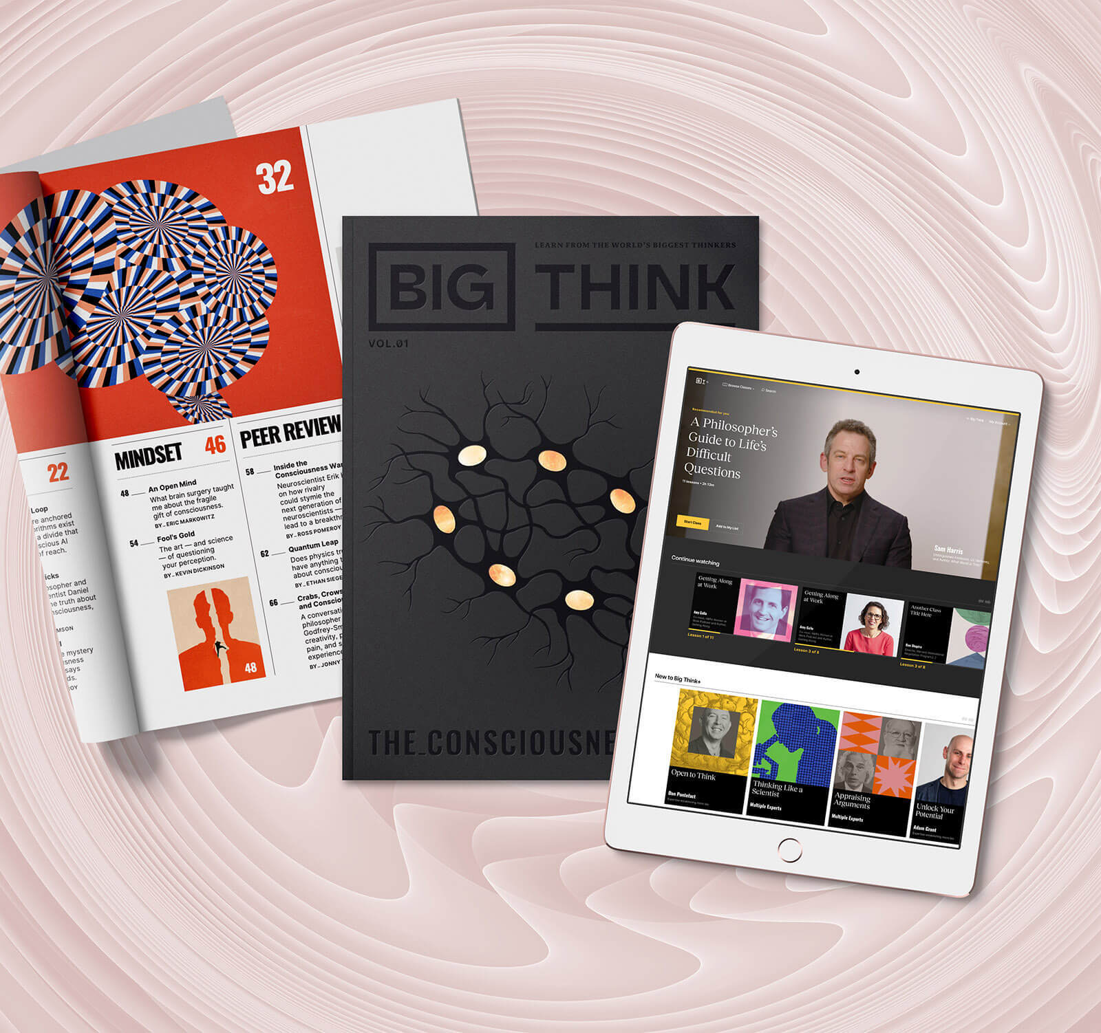 An open magazine, a closed Big Think "The Consciousness Issue," and a tablet displaying a website with various video thumbnails are arranged on a pink abstract background.